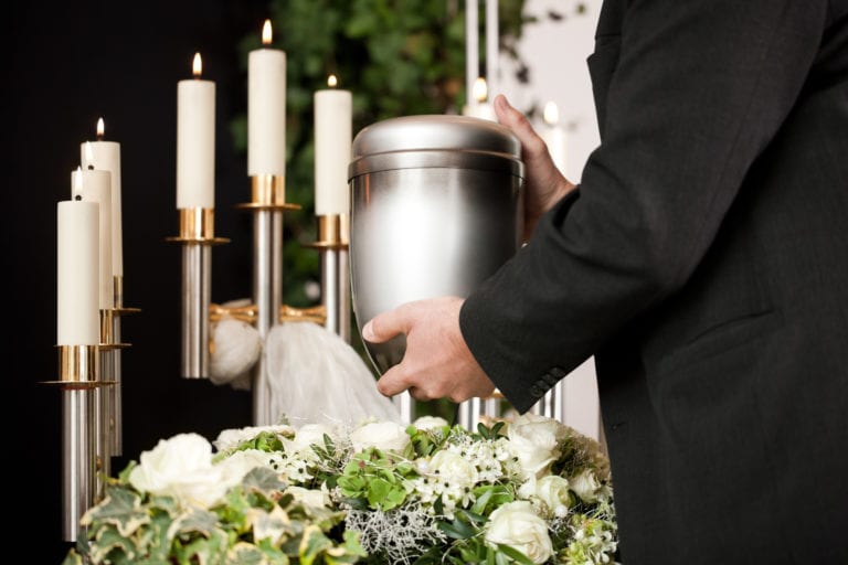 hombre llevando urna funeraria a un lecho de rosas blancas